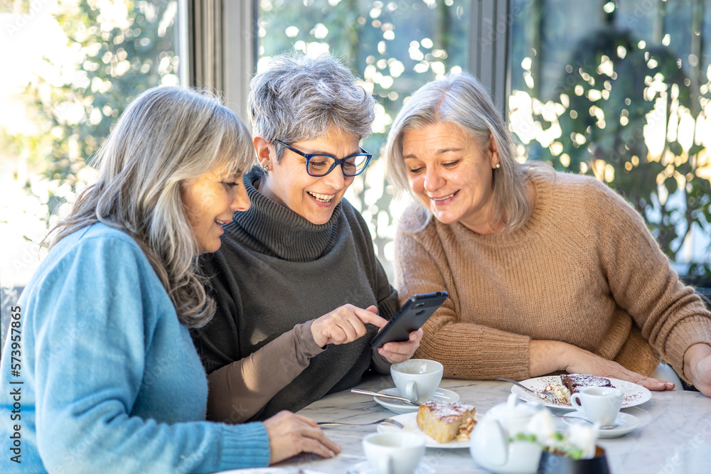© Andrea Vumbaca Photo - Group of 3 smiling mature female friends in white hats are using smartphone while at cafe having breakfast . Three senior women laugh look at the phone together © Andrea Vumbaca Photo - Group of 3 smiling mature female friends in white hats are using smartphone while at cafe having breakfast . Three senior women laugh look at the phone together