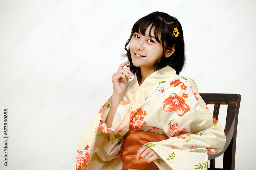 Beautiful young woman smiling and wearing traditional Japanese casual summer kimono or yukata, looking at camera on a chair with white background Beautiful young woman smiling and wearing traditional Japanese casual summer kimono or yukata, looking at camera on a chair with white background