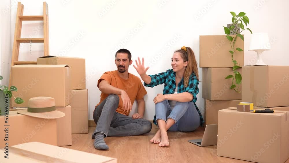 Happy couple moving home resting and talking in empty apartment with boxes making plans together and high five celebrating new life. Happy couple moving home resting and talking in empty apartment with boxes making plans together and high five celebrating new life.