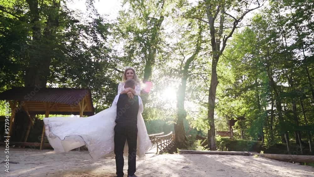 Groom spinning bride, holding her in his arms in the park in slow-motion Groom spinning bride, holding her in his arms in the park in slow-motion