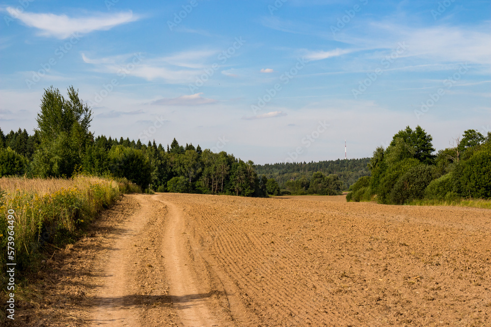 Country road along the edge of an agricultural field after plowing, rural landscape with cirrus clouds Country road along the edge of an agricultural field after plowing, rural landscape with cirrus clouds