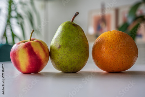 A pear, an orange and an apple laying upon a table