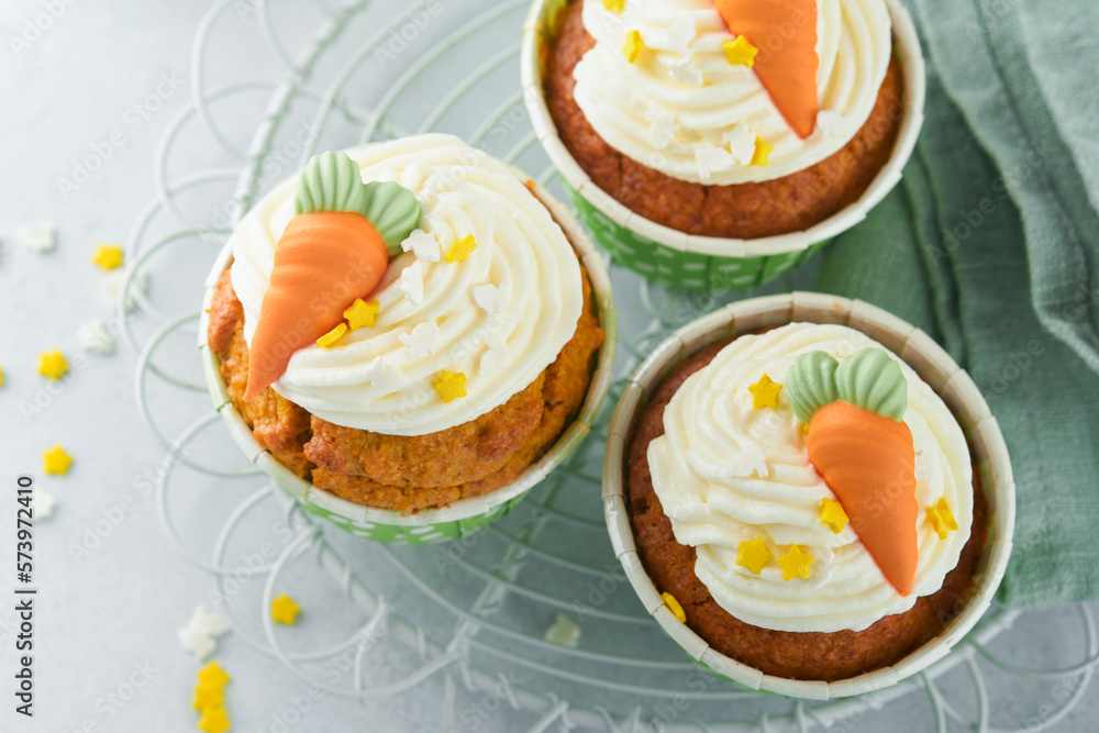 Carrot cake cupcakes for Easter. Carrot cupcakes with cream cheese frosting decorated with tiny marzipan carrots on white background. Happy Easter and spring holiday concept. Holydays homemade dessert Carrot cake cupcakes for Easter. Carrot cupcakes with cream cheese frosting decorated with tiny marzipan carrots on white background. Happy Easter and spring holiday concept. Holydays homemade dessert