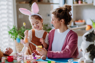 Happy mother with her little daughter decorating easter eggs.