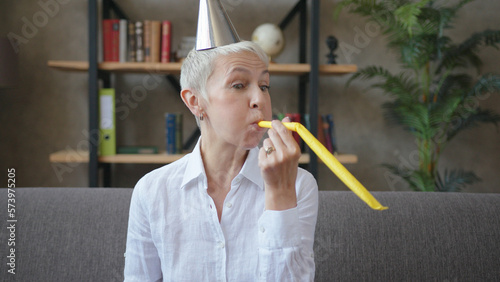 Happy business elderly woman in birthday cap blowing a whistle