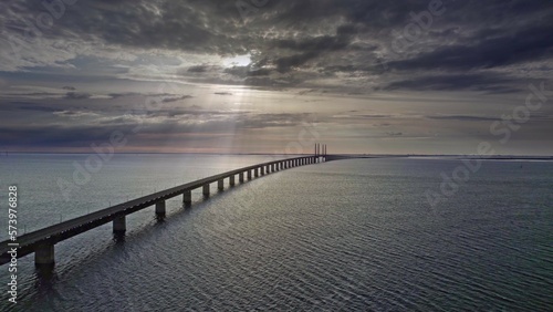 Aerial view high angle of the colorful sunset, the sun rays breaking through the dark dramatic clouds sky over the sea, calm waves. At the bridge over the Öresund strait between Sweden and Denmark