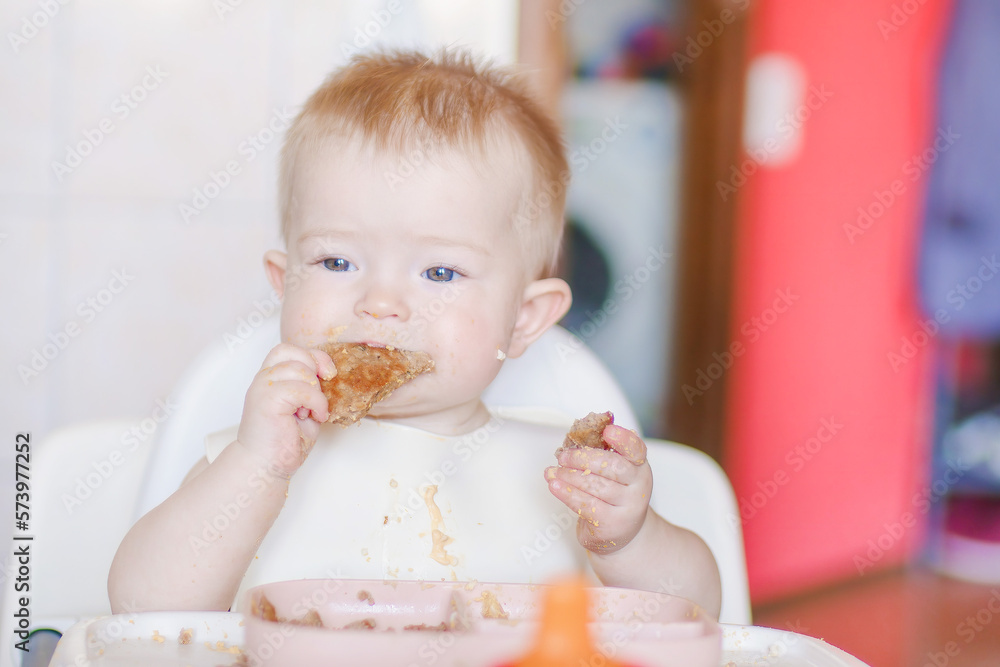 Funny child gets dirty with food. Happy childhood and delicious food. Close-up of a child's face. Little cute kid eats with his hands. Grimaces of a cheery baby Funny child gets dirty with food. Happy childhood and delicious food. Close-up of a child's face. Little cute kid eats with his hands. Grimaces of a cheery baby