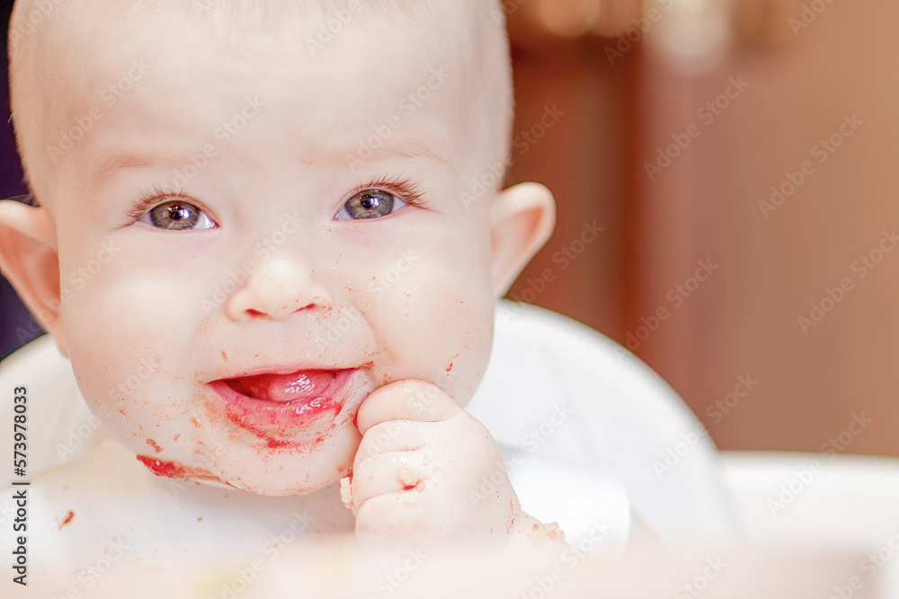 Grimaces of a cheery baby. Funny child gets dirty with food. Happy childhood and delicious food. Close-up of a child's face. Little cute kid eats with his hands Grimaces of a cheery baby. Funny child gets dirty with food. Happy childhood and delicious food. Close-up of a child's face. Little cute kid eats with his hands
