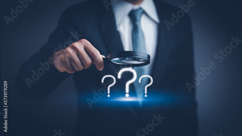 businessman hand holding a magnifying glass with question mark icon , concept of analyzing problem Or find the cause that occurs during the work process photo