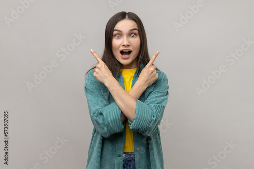 Surprised woman with dark hair standing with crossed hands and pointing to copy space on both sides.