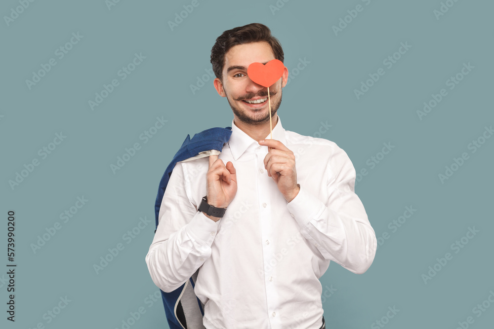 Happy smiling delighted joyful man with mustache covering his eye with red heart on stick. Happy smiling delighted joyful man with mustache covering his eye with red heart on stick.
