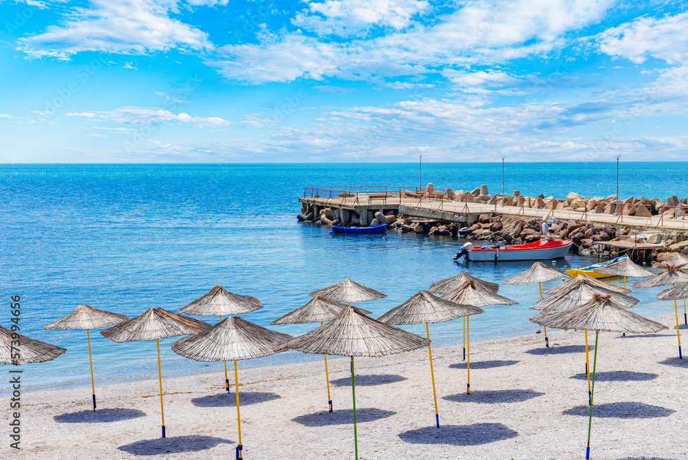 Obraz premium Straw beach umbrellas and sun loungers for relaxing by the sea.