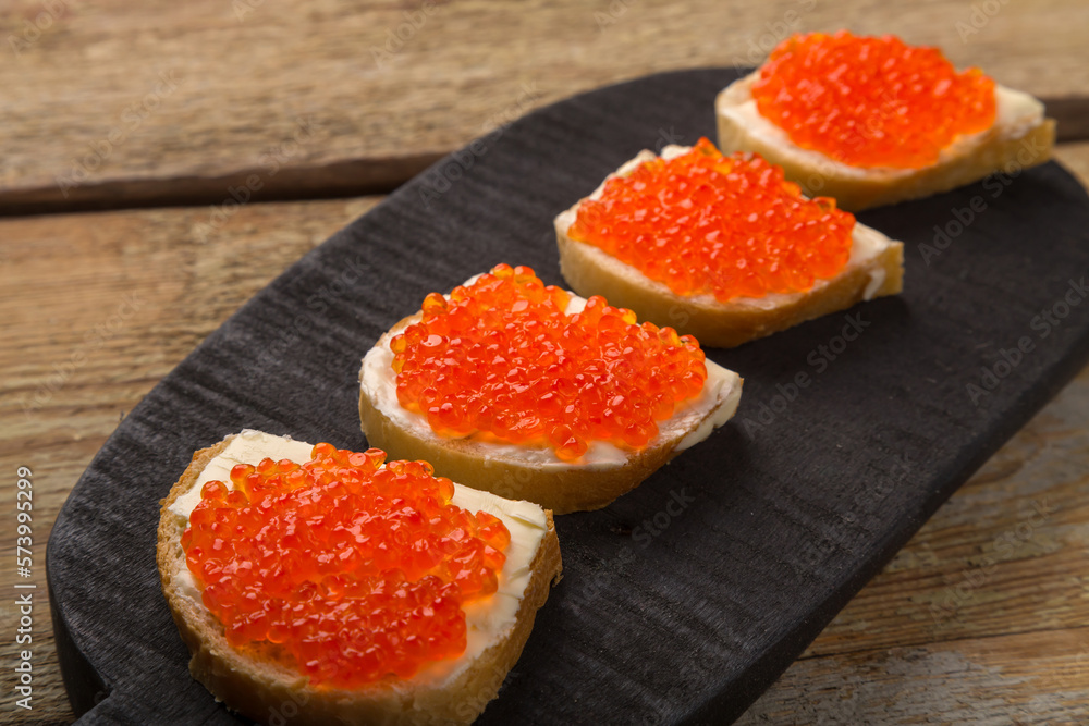 Toasts with red caviar and butter on a black serving board on a wooden table. Toasts with red caviar and butter on a black serving board on a wooden table.