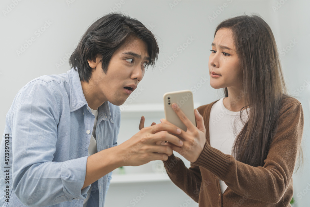Infidelity, suspicion asian young couple love fight relationship, wife holding cellphone, smartphone cheating on phone, scolding husband about mistrust, distrust and jealousy when sitting at home. Infidelity, suspicion asian young couple love fight relationship, wife holding cellphone, smartphone cheating on phone, scolding husband about mistrust, distrust and jealousy when sitting at home.