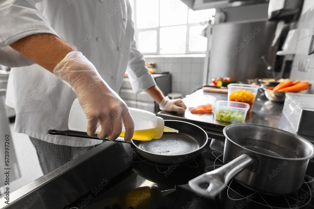 cooking food, profession and people concept - close up of male chef pouring oil to frying pan at restaurant kitchen cooking food, profession and people concept - close up of male chef pouring oil to frying pan at restaurant kitchen