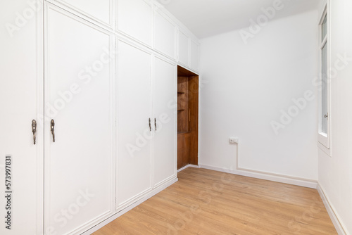 Built-in spacious wardrobes in a room with wooden laminate flooring. Concept of organizing storage and laconic interior