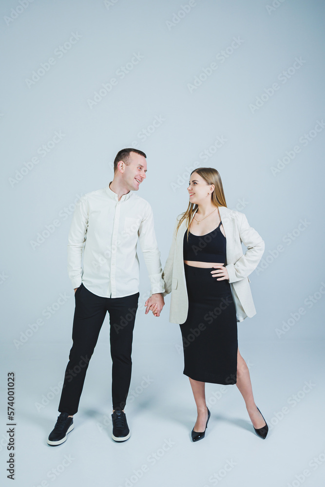 Fototapeta premium Beautiful young couple in love hugging on a white background. A stylish couple embraces and enjoys feelings. Men and women in stylish casual clothes