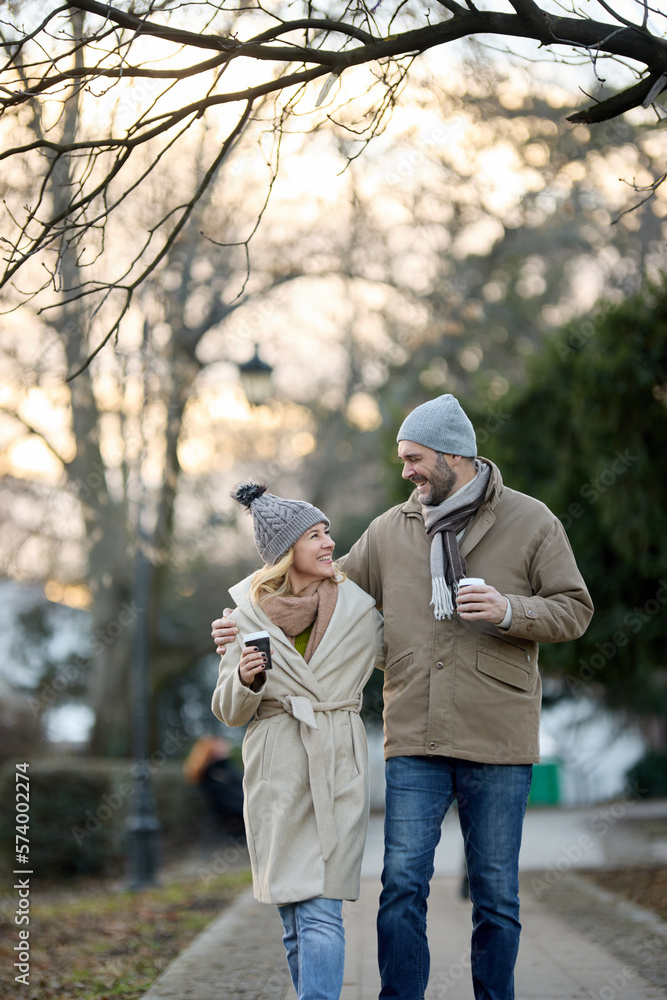 Fototapeta premium A happy romantic couple with coffee walking outdoors in the park