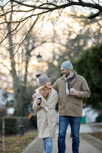 A happy romantic couple with coffee walking outdoors in the park