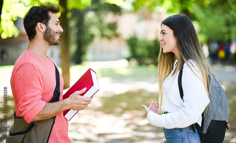 Two students, male and female, talking outdoor in a college park while holding books Two students, male and female, talking outdoor in a college park while holding books