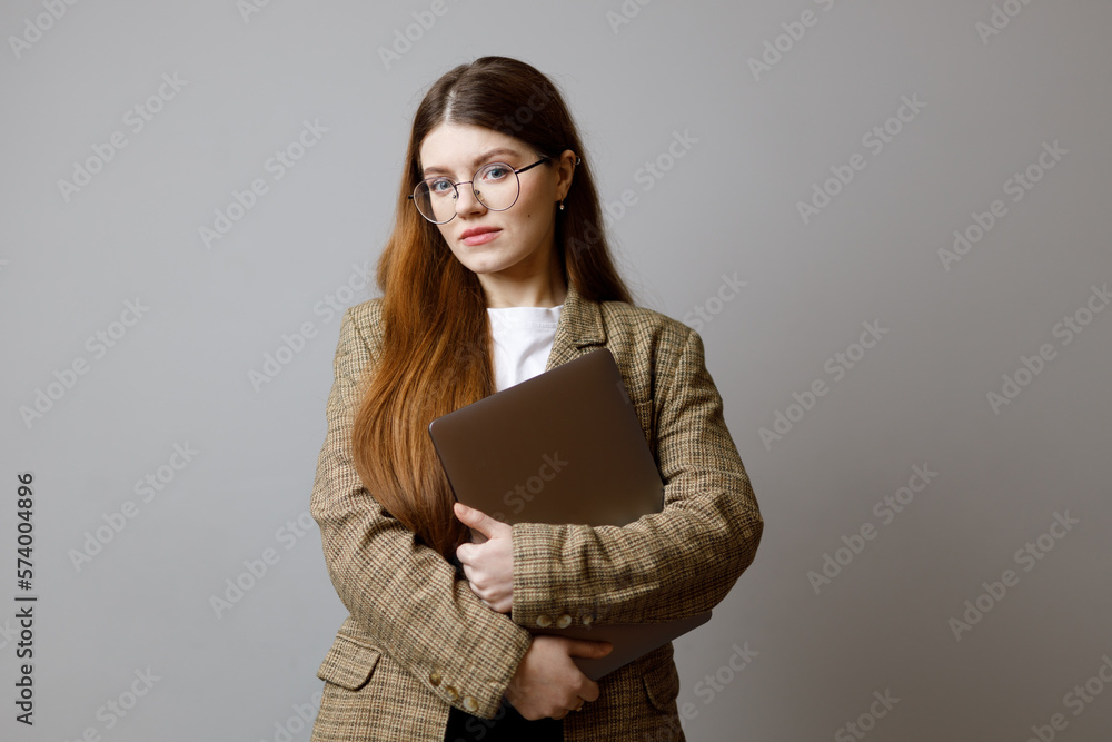 Business woman in a jacket with a laptop on a gray background.