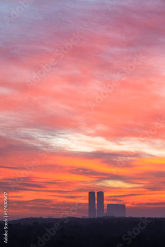 red clouds in dawn sky over city park and towers on cold morning