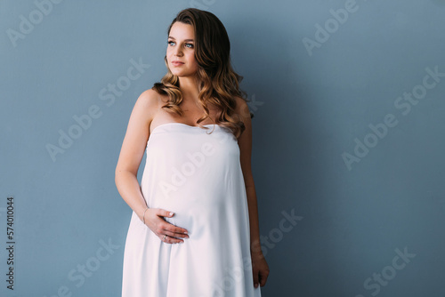 beautiful pregnant woman with beautiful white silk fabric. Studio photo on the background of a white wall © Ivan