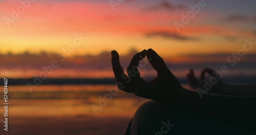 Woman does yoga at dawn on ocean. Silhouette of woman's hands. Meditation, practice of zazen in Buddhism. Calming body, contemplating, enlightenment. Gesture of index and thumb connected in ring.