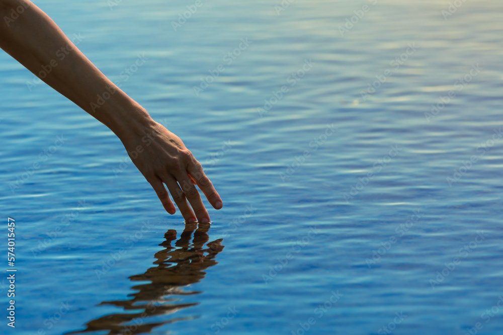 Woman's hand touching calm water surface. Feeling of peace and zen in nature. 