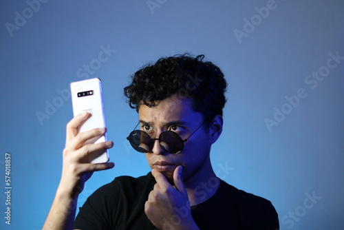 joven latino viendo su teléfono inteligente posando en un fondo azulado