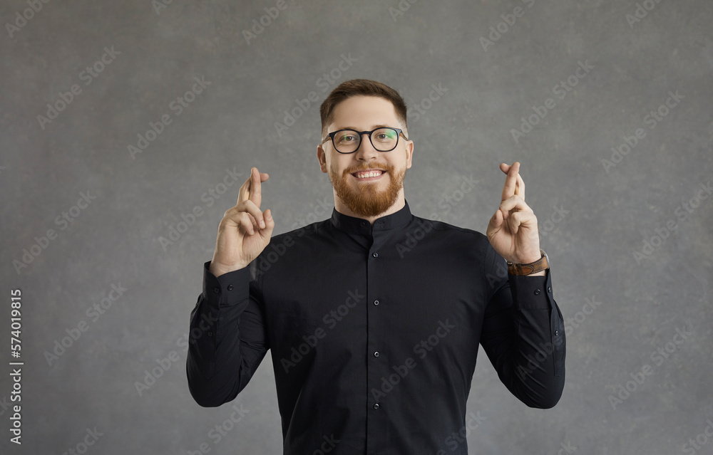 Portrait of a happy joyful man with a sense of hope crossing his fingers dreaming about something. Smiling cheerful caucasian man stands on a gray concrete background and hopes for the best miracle. Portrait of a happy joyful man with a sense of hope crossing his fingers dreaming about something. Smiling cheerful caucasian man stands on a gray concrete background and hopes for the best miracle.