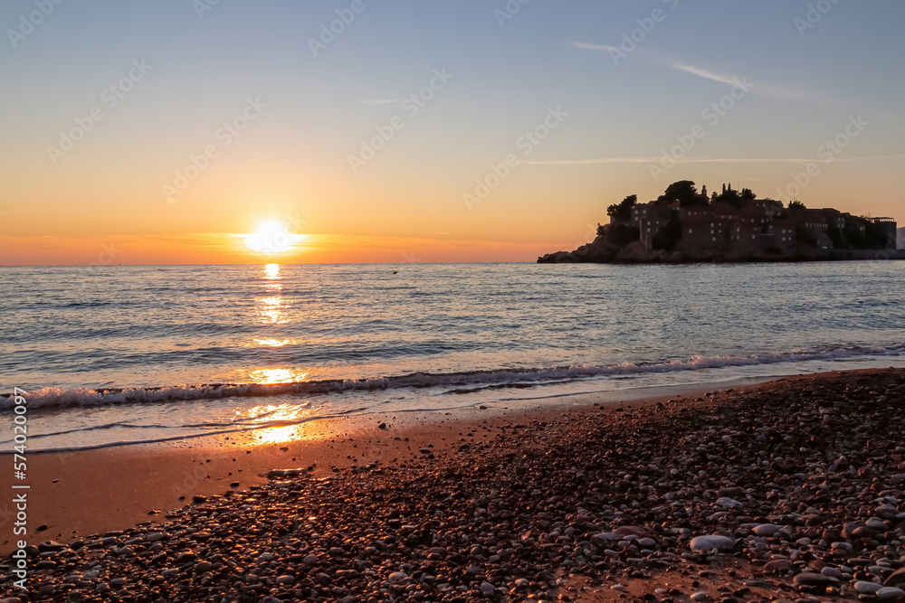 Scenic sunset view from Sveti Stefan Beach at Adriatic Mediterranean Sea, Budva Riviera, Montenegro, Europe. Reflection of sun beams on water surface during twilight. Summer vacation in seaside hotel Scenic sunset view from Sveti Stefan Beach at Adriatic Mediterranean Sea, Budva Riviera, Montenegro, Europe. Reflection of sun beams on water surface during twilight. Summer vacation in seaside hotel