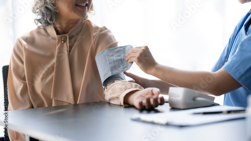 Asian female doctor measuring blood pressure for an elderly female patient.