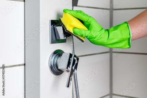 фотографія Close-up of a woman wearing green rubber gloves cleaning a shower cabin with a s