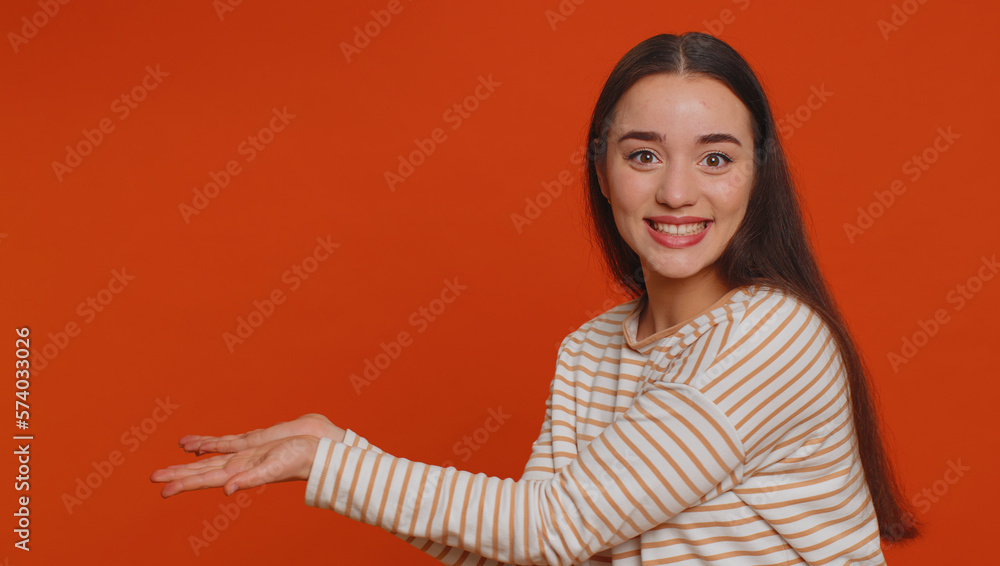 Lovely millennial pretty woman showing thumbs up and pointing empty place, advertising area for commercial text, copy space for goods promotion. Young girl. Studio shot indoors on red wall background Lovely millennial pretty woman showing thumbs up and pointing empty place, advertising area for commercial text, copy space for goods promotion. Young girl. Studio shot indoors on red wall background
