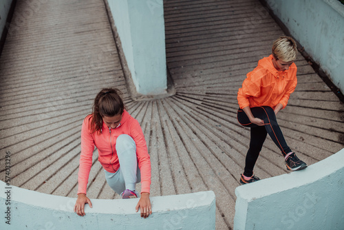 Two women warming up together and preparing for a morning run in an urban environment. Selective focus 