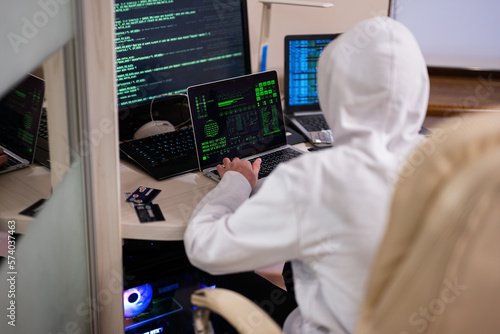 Boy hacker fraudulently use credit card for payment. Internet theft . Man wearing a balaclava and holding a credit card while sat behind a laptop.