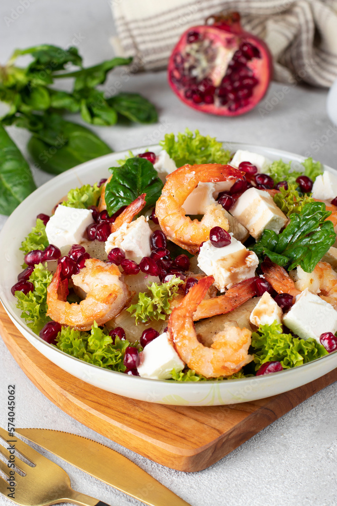 Salad with shrimps, pineapple, feta and pomegranate seeds in a plate on green lettuce leaves, on wooden board