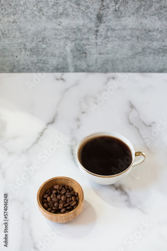 Aamekin of roasted coffee beans sits next to a coffee in a teacup. © Danielle Motif