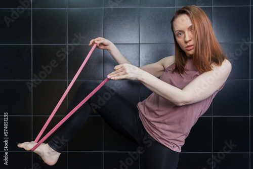 A woman in sportswear holding measuring tape, dark tiles in the background. Sport and recreation concept.