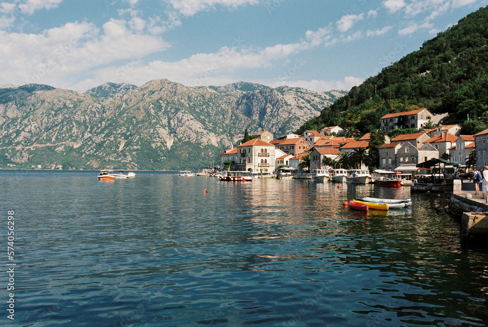 Boats moored at the pier of Perast with old houses at the foot of the mountains