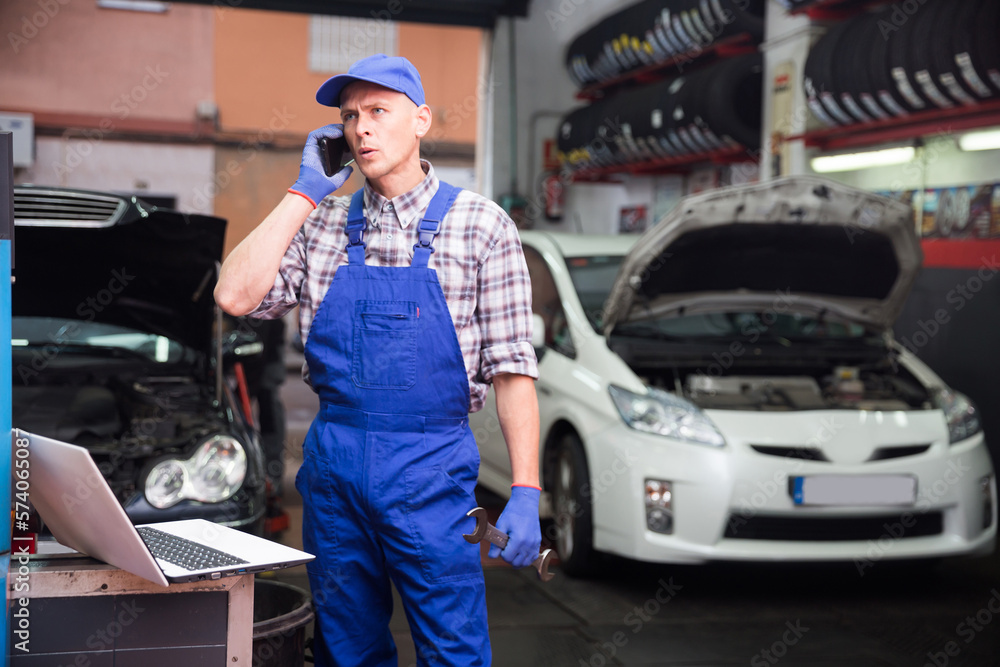 Professional car mechanic calls on smartphone to client in auto repair service