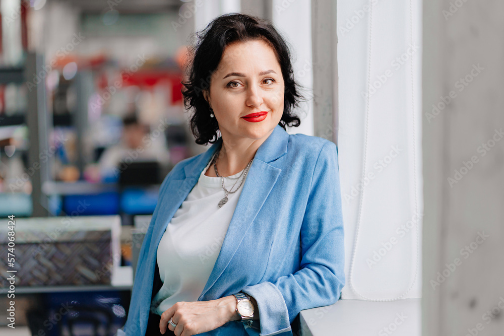 a brunette woman in a blue jacket in a workspace by the window