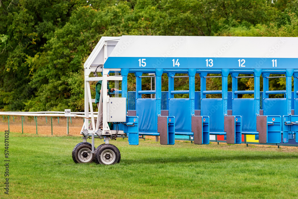 Blue horse racing starting gate on start by tractor machine at equiestrian racehorse hippodrome. Outdoor sport racecourse competition equipment