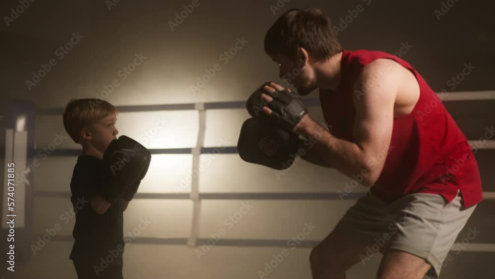 Portrait of a little boy having a sparring with his coach in a boxing ring. Close-up view of a kid preparing for the competition while exercising in local fitness club. High quality 4k footage Portrait of a little boy having a sparring with his coach in a boxing ring. Close-up view of a kid preparing for the competition while exercising in local fitness club. High quality 4k footage