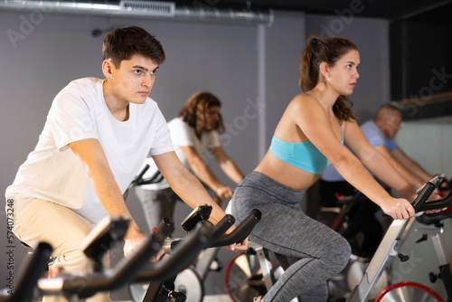 Men and woman taking indoor cycling class at fitness center, doing cardio riding bike