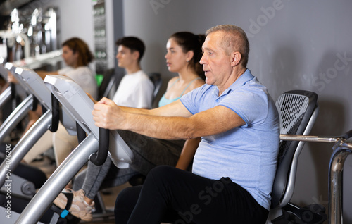 Concentrated elderly man working out on stationary bicycle in gym. Concept of healthy lifestyle of senior generation