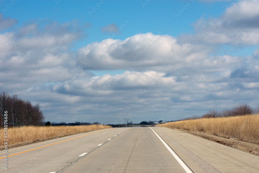 An empty interstate with a blue sky and white clouds. 