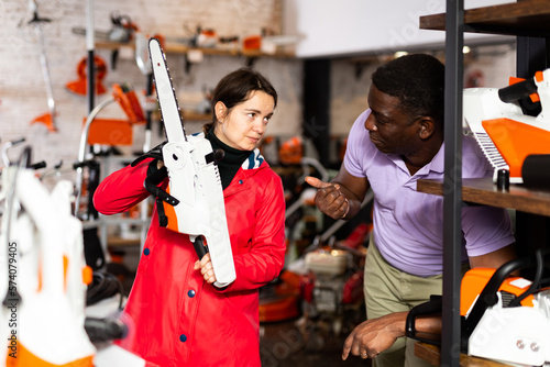African-american man consulting Caucasian woman about chainsaw in gardening tools shop.