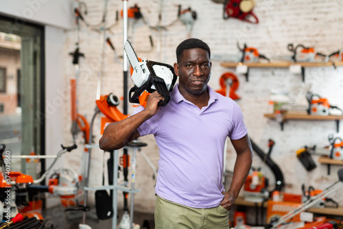 African-american man with chainsaw standing in gardening tool store.